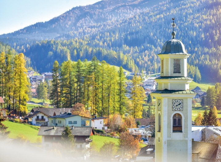 Der Kirchturm von Sexten vor grünen Wäldern in Südtirol